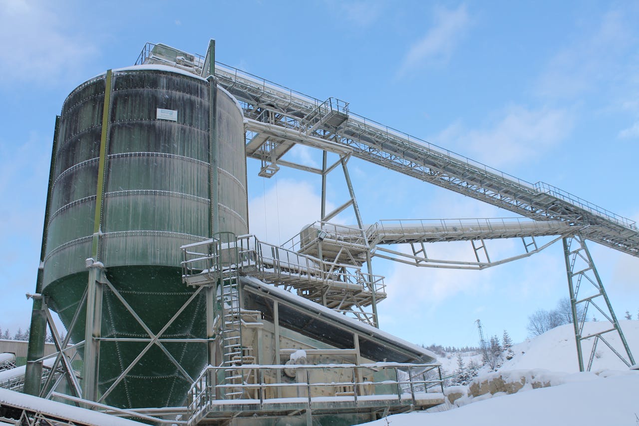 service-02 A snow-covered industrial plant with silo and machinery under a blue sky.