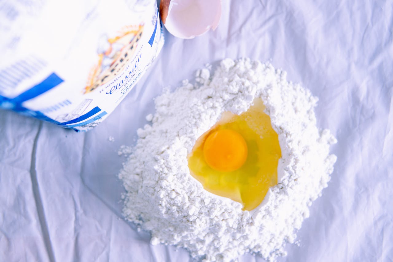A fresh egg nestled in flour, ready for homemade pasta preparation, flat lay.